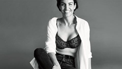 A woman smiling showing her bra in a white shirt and jeans